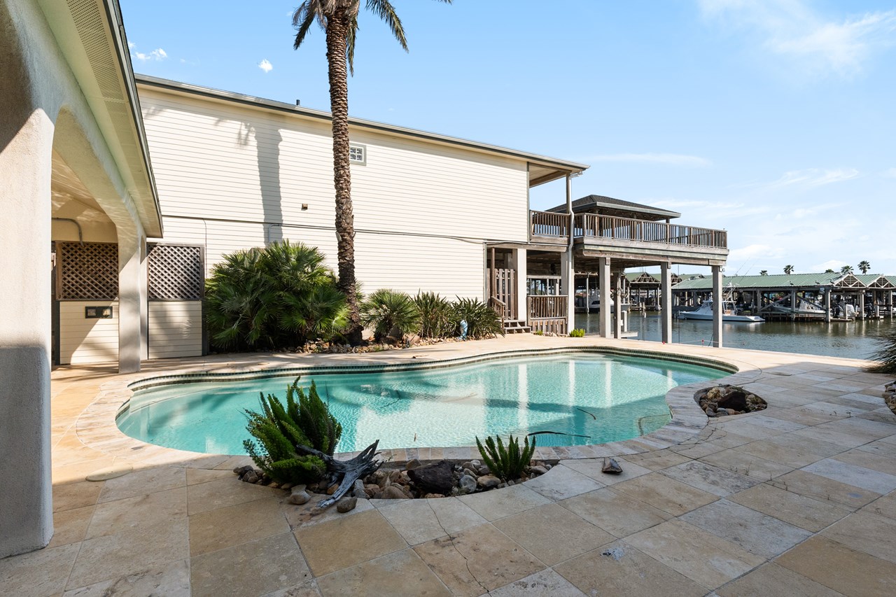 swimming pool area with a covered sitting area to your left you can see the steps leading up to the closed gate between the main home and the swimming pool.  what an inviting place to sit in the morning or evening with a view of the harbor sharing all your fishing stories.